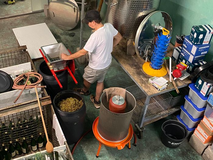 Die Weinpresse (orangener Fuß) wartet auf die Maische (im schwarzen Fass)